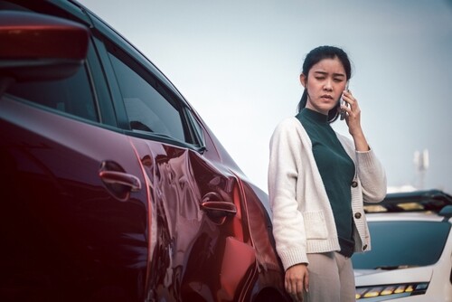 Young woman standing beside damaged car after traffic collision on roadside