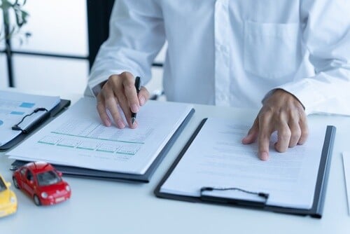 Businessman signing car insurance document beside toy vehicle and claim form
