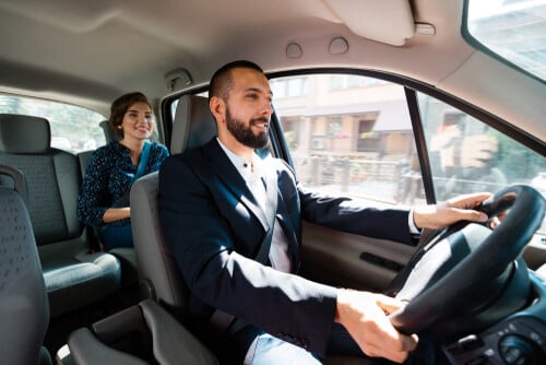 smiling male driver in suit steering vehicle with female passenger in backseat
